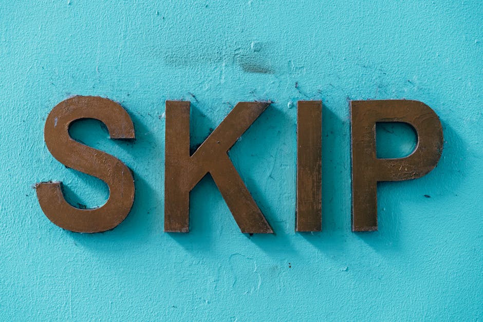 A close-up view of three large, uppercase metal letters spelling 'SKIP' mounted on a vibrant turquoise wall with a textured finish. The letters have a matte, dark brown finish, showing slight signs of